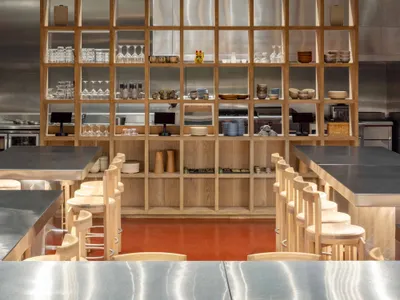 A modern restaurant bar featuring wooden shelves, stainless steel appliances, and ceramic bowls and plates.