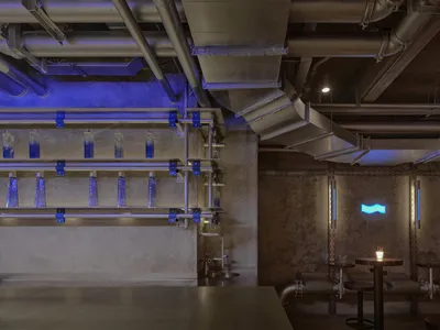 An industrial-style restaurant interior with metal pipes, concrete walls, and blue lighting.