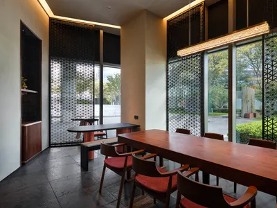 Modern restaurant interior with wooden tables, red cushioned chairs, and glass partitions.