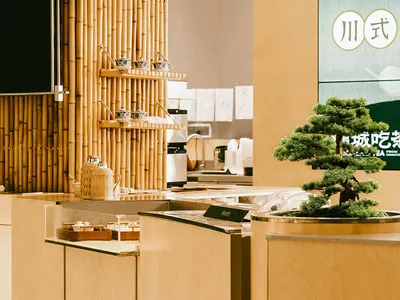 A wooden restaurant interior with a bamboo backdrop and bonsai tree.