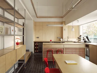 An interior view of a cafe featuring wood plywood walls and counters, red stools, and a black and white tiled floor.