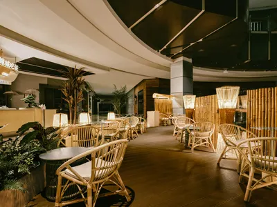 一間空蕩、時尚的室內餐廳酒吧，擺設藤編家具、盆栽植物與竹製燈飾。