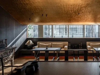 Modern industrial-style restaurant interior with metallic ceiling tiles, minimalist furniture, and large windows.