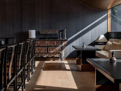 Modern restaurant lounge with dark wooden furniture, glass walls, and steel accents.