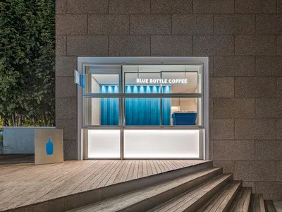Modern coffee shop exterior with concrete walls and illuminated windows.