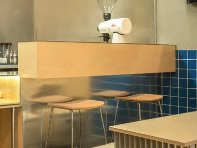 Modern wooden coffee shop bar counter with stools and espresso grinder.