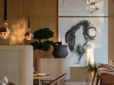 A modern restaurant interior with wooden walls, hanging lamps, and abstract paintings.