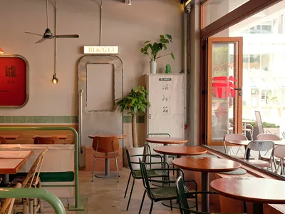 Cafe interior with wooden furniture, green plants, and industrial-style decor.