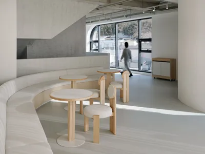A minimalist restaurant seating area with white fabric seating and wooden tables.