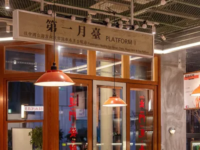 Industrial-style restaurant interior with wooden tables and chairs, red pendant lights, and sign indicating 'Platform 1'.