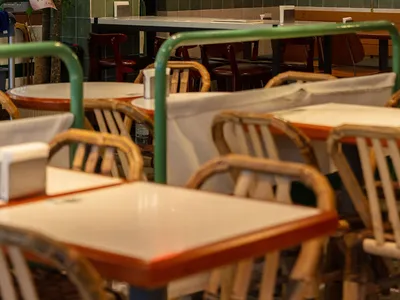 A rustic restaurant interior with wooden tables, metal railings, and green plants.