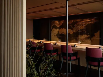 A modern restaurant interior featuring wooden panels and marble accents with red chairs and a large dragon artwork on the bac