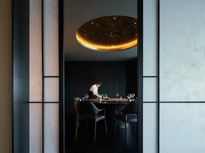 A modern restaurant interior featuring a black metal dining table with surrounding chairs and a circular light fixture in the