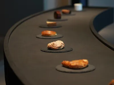 黑色花崗岩餐檯上設有輸送帶，展示各式糕點與麵包。