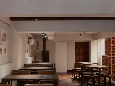 A photograph of an industrial-themed restaurant interior with wooden tables and chairs, white walls, and exposed ceiling beam