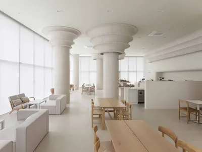 A minimalist restaurant/cafe with clean concrete floors and wooden furniture, featuring large windows and open seating.