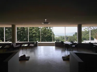 Modern restaurant interior with extensive glass window walls providing ample sunlight and a glimpse of the sea and lush green