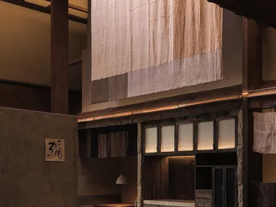 An industrial-themed restaurant interior with wooden tables, stone walls, and fabric curtains.