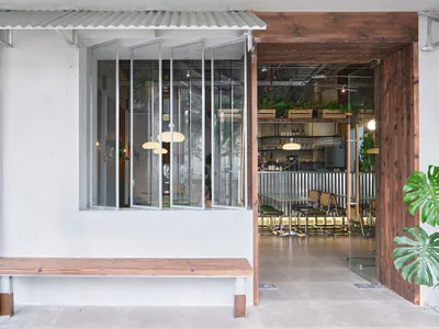 A modern cafe bar featuring metallic and wooden interior design with white walls and green plants.