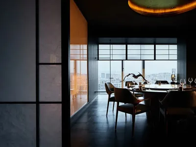 Modern restaurant interior with dark wood flooring and large windows overlooking a cityscape.