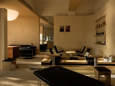 Modern restaurant interior with wooden and concrete seating, black leather accents, and minimalist design.