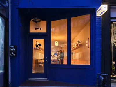 藍色店面搭配大型落地窗，透露出溫暖的室內燈光與燈具。