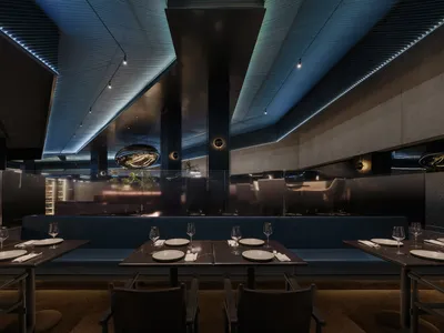 Modern, industrial restaurant interior with exposed metal ceiling, concrete walls, and glass partitions.