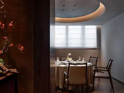 A modern restaurant interior featuring a table set with white tablecloth, chairs, and floral centerpiece.