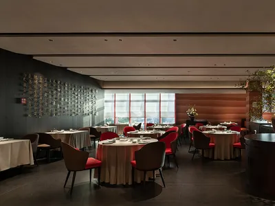 A modern restaurant interior with marble walls, glass tables, and fabric chairs.