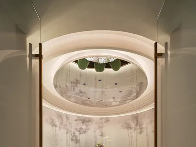 Modern restaurant with a sculptural ceiling and green chairs surrounding a round table set for dining.