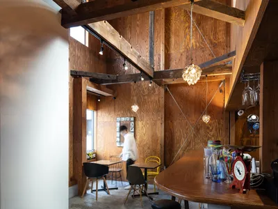 Industrial-style restaurant interior with wooden beams, tables, stools, and a bar area.