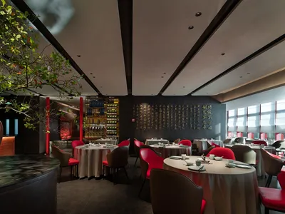 Modern restaurant interior with tables set for dining, red chairs, and a large tree in the corner.