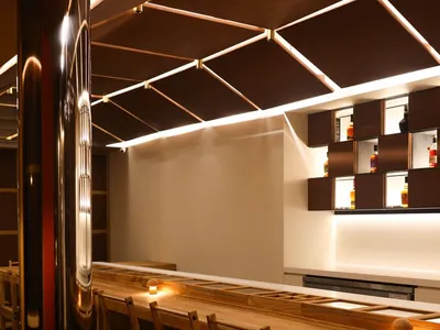 A modern restaurant bar with wooden seating and illuminated shelves.