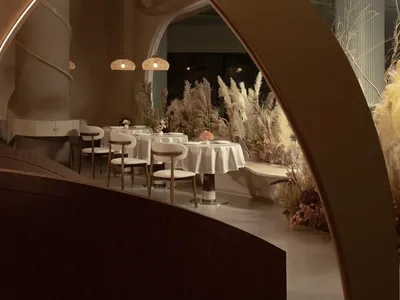 A modern restaurant interior with minimalist design, featuring white walls, wooden elements, and natural light.