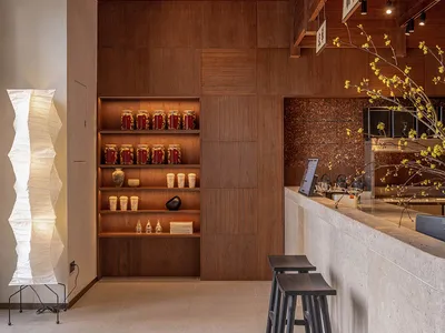 A modern restaurant interior with wooden shelves displaying jars and cups, bar counter with stools, and a white paper lantern