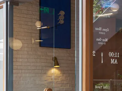 A cozy restaurant interior with wooden tables and chairs, a warm light fixture, and a brick wall.