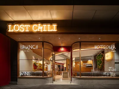 A modern, illuminated storefront with a neon sign reading 'LOST CHILI' and windows displaying the words 'BRUNCH', 'HOT SOUR',