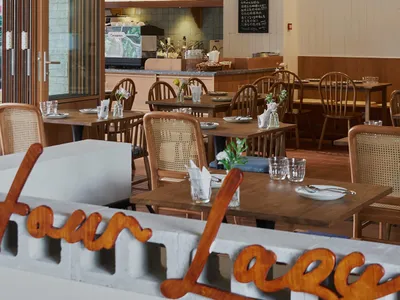 Modern restaurant dining area with wooden tables and chairs, brick walls, and concrete flooring.
