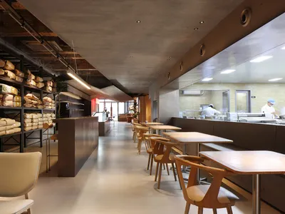 A spacious, industrial-style restaurant interior with concrete flooring, wooden furniture, and open seating.