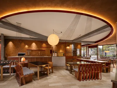 Industrial design restaurant bar with wooden tables and chairs, exposed concrete ceiling beams, and warm lighting.