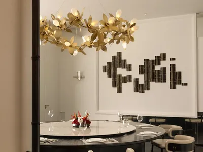 Modern restaurant dining room with metallic chandelier and circular table setup with chairs and wine glasses.