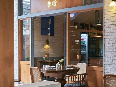 A modern restaurant interior featuring wooden tables, brick walls, and glass windows.