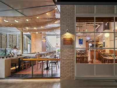 Modern restaurant interior with wooden tables, brick walls, and glass windows.