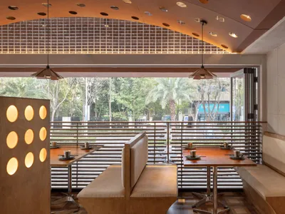A modern restaurant interior featuring wooden tables, metallic lighting, and a seamless blend of materials.