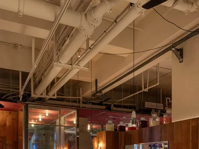 Interior of an industrial-themed restaurant with wooden tables, concrete floor, and metallic pipes overhead.