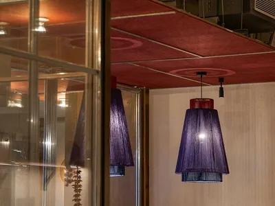 An industrial-style restaurant interior featuring wooden tables and chairs with purple fabric lighting shades.