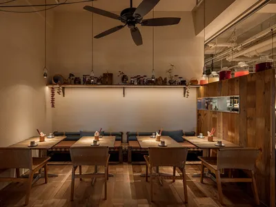 Interior view of an industrial-style restaurant with wooden flooring and furniture, featuring tables and chairs, and a shelf