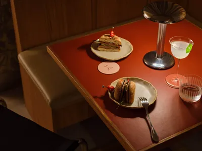 Serving of a sandwich and a cocktail on a wooden table in a restaurant setting.