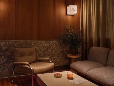 An industrial-style living room with wooden walls and furniture, featuring a couch, armchair, and coffee table with a drink a