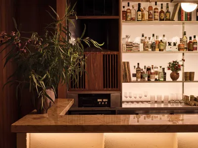 Modern, minimalist restaurant bar interior with marble countertop, wooden shelving, and a variety of drinks.